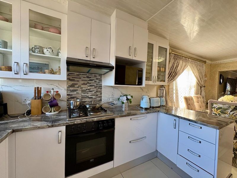 A well-maintained kitchen featuring white cabinetry, stone-look countertops, a gas hob with extractor, and a mosaic tile backsplash, offering a functional and bright workspace.