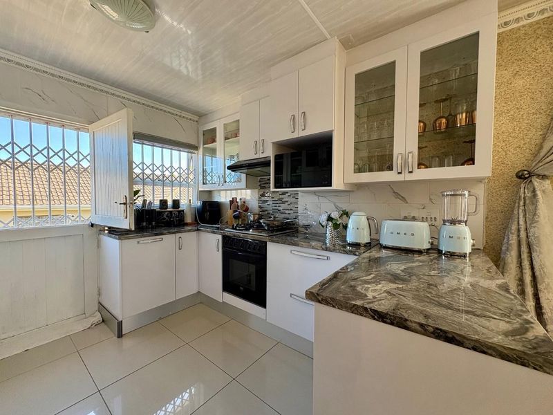 A well-maintained kitchen featuring white cabinetry, stone countertops, built-in oven and hob, and tiled flooring with direct access to an exterior security door.