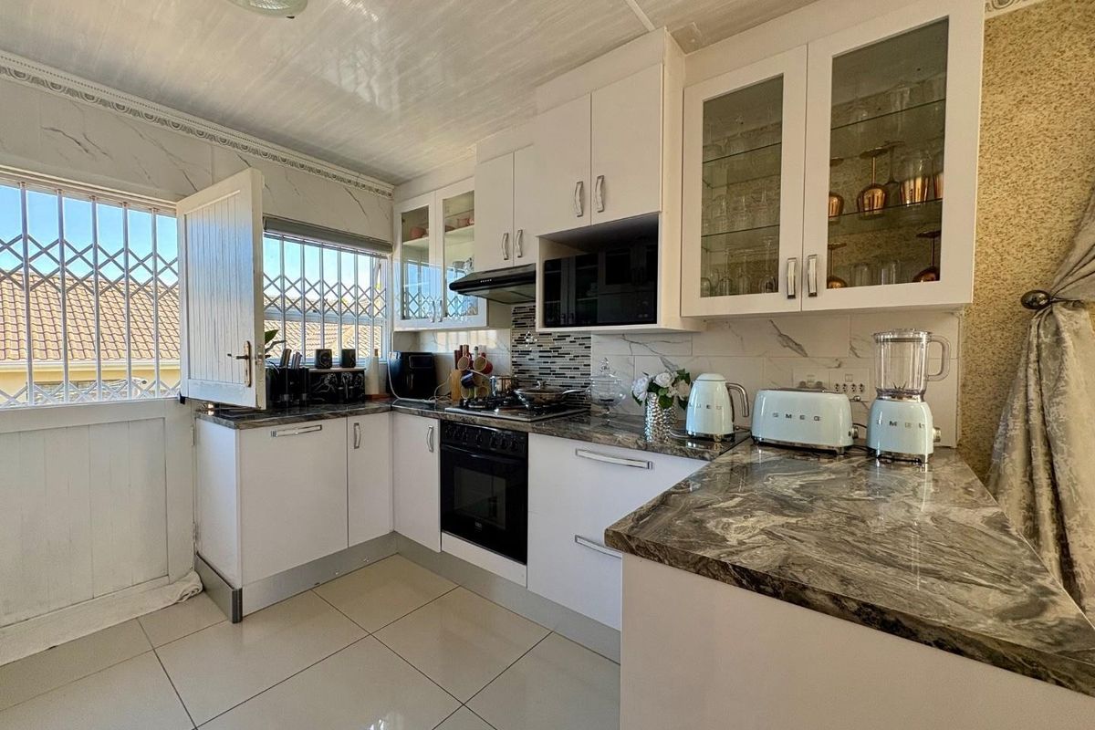 A well-maintained kitchen featuring white cabinetry, stone countertops, built-in oven and hob, and tiled flooring with direct access to an exterior security door.