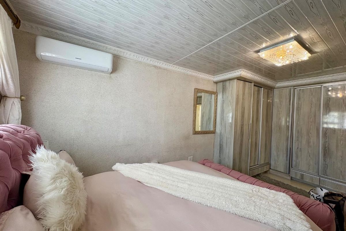 A bedroom featuring built-in cupboards, decorative ceiling paneling, and a wall-mounted air conditioning unit.