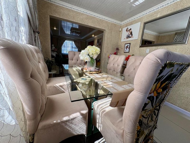 A dining room featuring decorative ceiling cornices and tiled flooring, with an open-plan layout connecting to the adjacent living area.