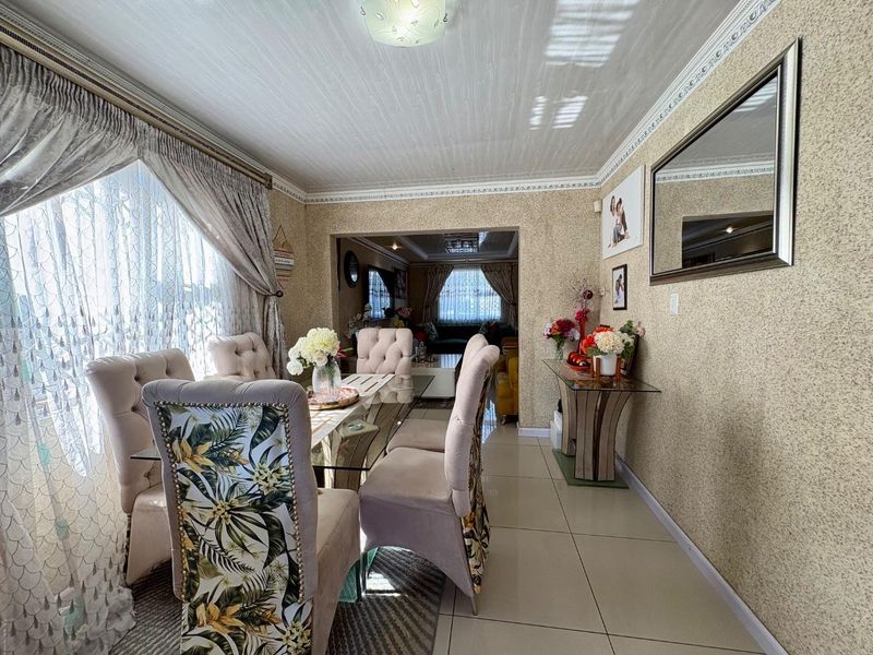 A dining room featuring tiled flooring and decorative crown molding, with an open-plan layout connecting to the adjacent living area.