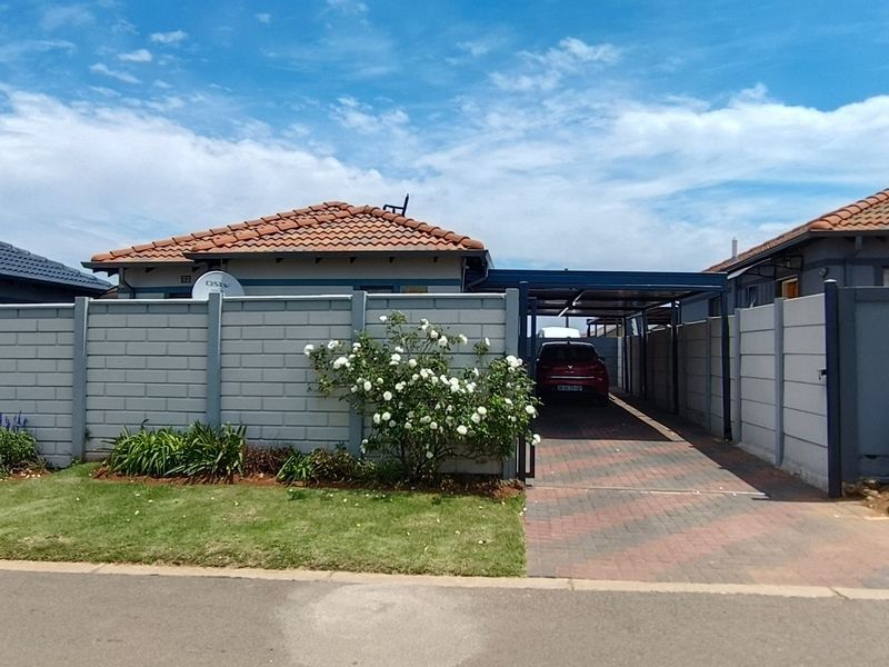 Front exterior view of the property featuring a paved driveway, carport, and concrete block boundary wall with a well-maintained lawn.