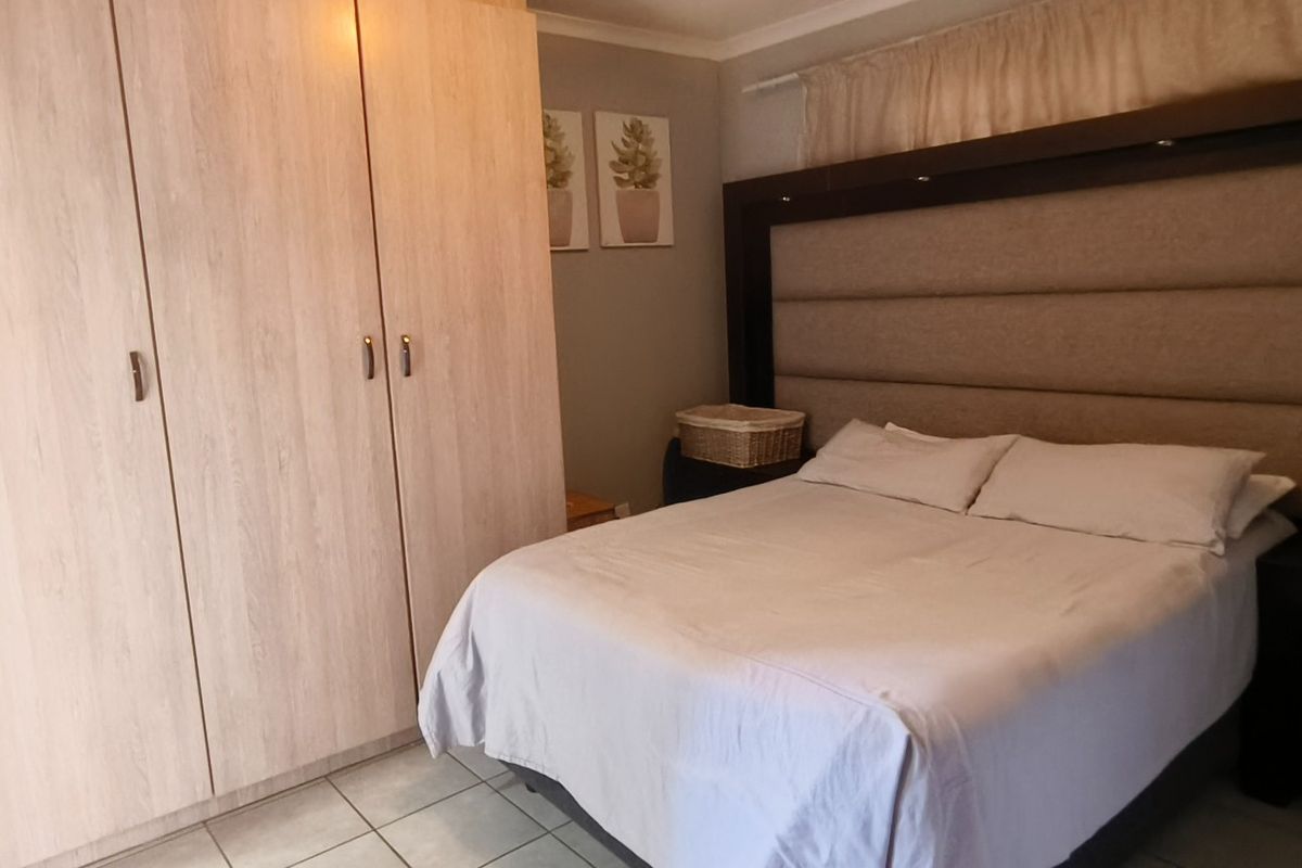 A well-maintained bedroom featuring built-in wardrobes, tiled flooring, and a large integrated headboard with built-in lighting.