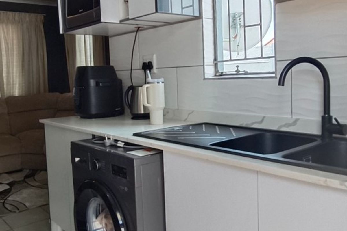 A modern kitchen featuring sleek cabinetry, a dark integrated sink with a contemporary faucet, tiled backsplash, and tiled flooring.