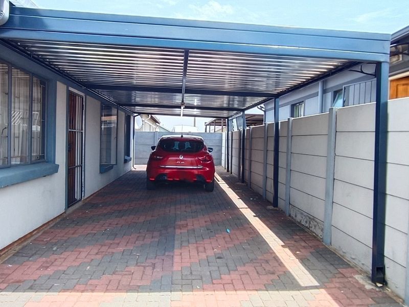 A covered carport area featuring a paved driveway and secure precast concrete boundary walling.