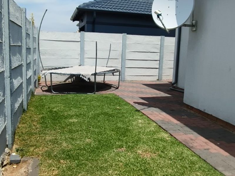 A rear exterior view featuring a small lawn, paved walkway, and perimeter precast concrete walling.