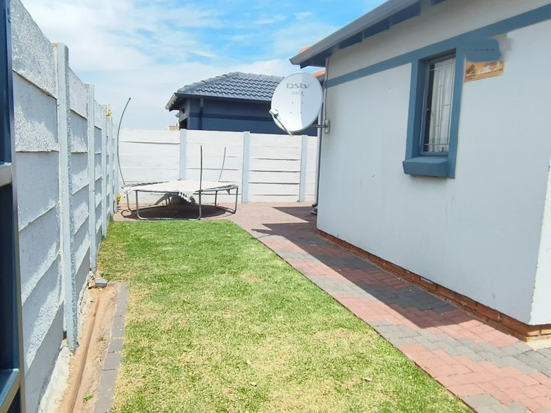 A side garden area featuring a paved walkway, precast concrete boundary wall, and exterior wall access with a satellite dish installation.