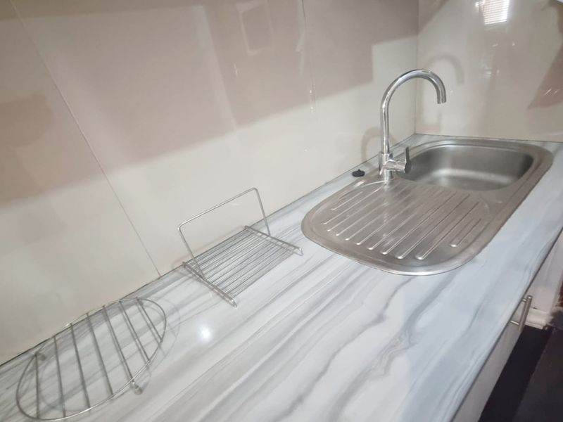 A compact kitchen area featuring a stainless steel sink, modern faucet, and marble-effect laminate countertop with a clean tiled splashback.