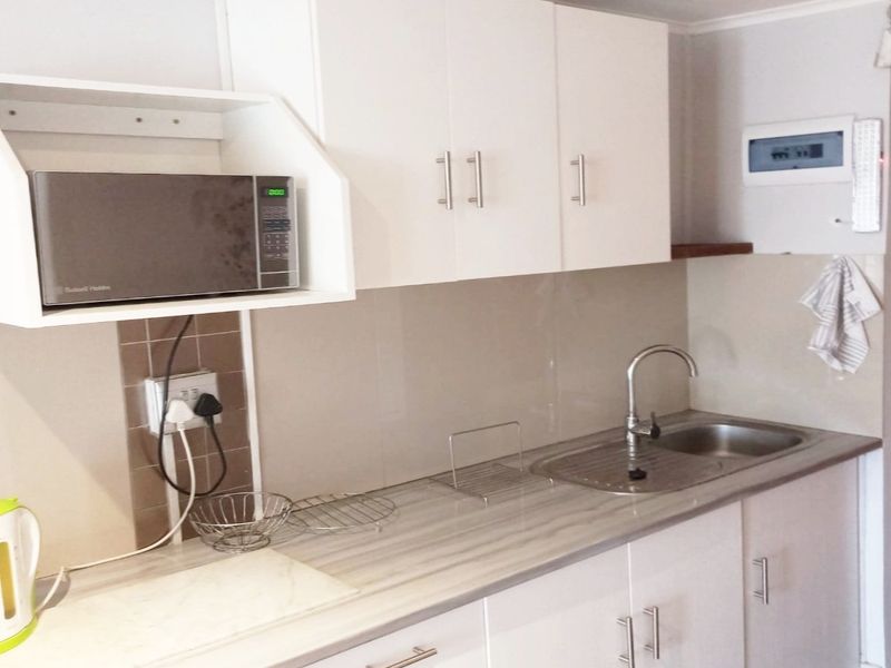 A compact kitchen featuring white cabinetry, a laminate countertop, stainless steel sink, and a dedicated shelf for a built-in microwave.