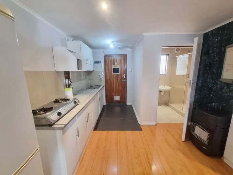 A functional kitchen featuring white cabinetry, a gas hob, and laminate flooring, with direct access to an adjacent bathroom.