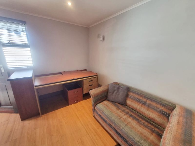 A functional bedroom featuring laminate flooring, a window with fitted blinds, and neutral wall finishes, suitable for use as a bedroom or home office.