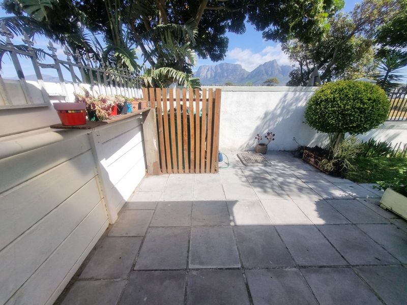 A paved outdoor patio area featuring a boundary wall, metal fencing, and a wooden gate, offering a pleasant view of the surrounding landscape.