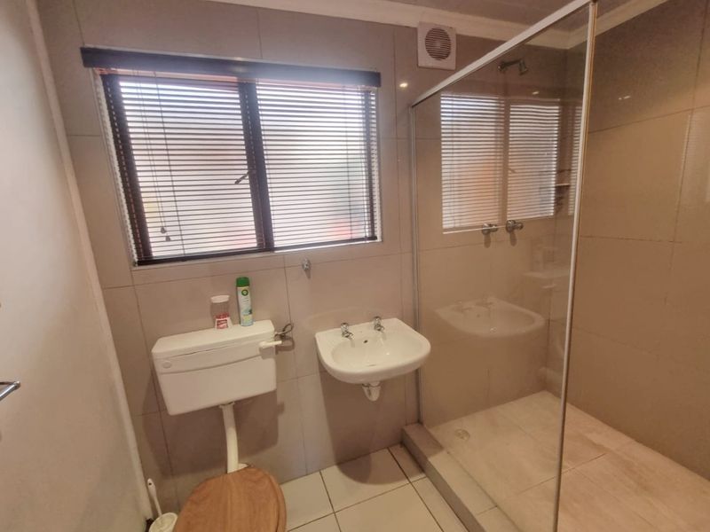 A functional bathroom featuring a glass-enclosed shower, wall-mounted basin, and toilet with neutral wall and floor tiling.