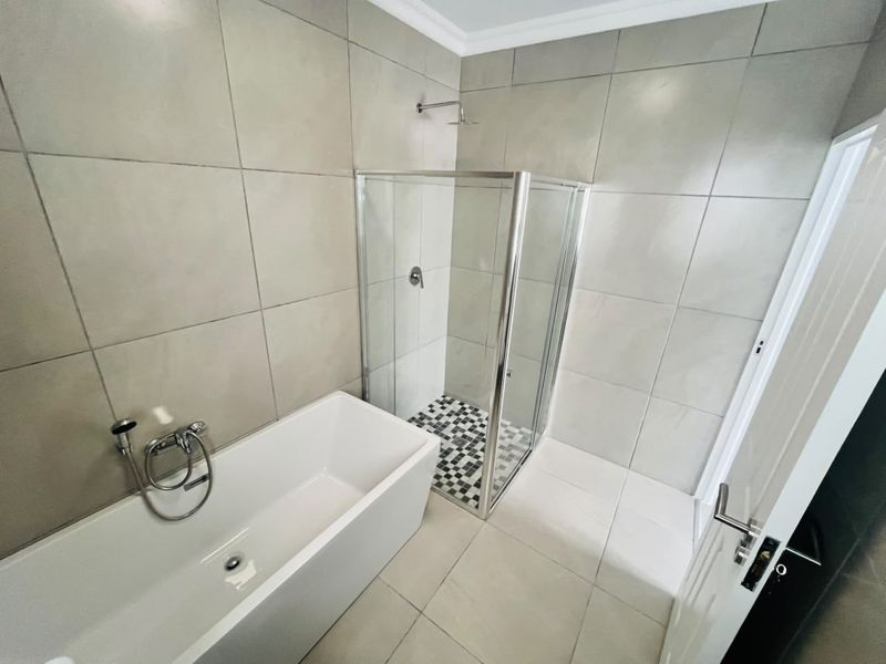 Modern bathroom featuring a sleek freestanding bathtub, a separate glass-enclosed shower, and neutral large-format wall and floor tiling.