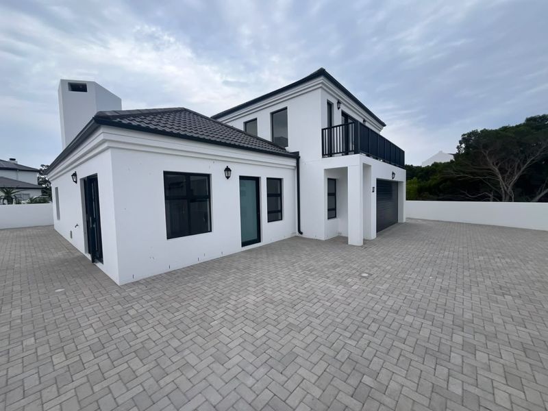 Modern two-story house featuring a clean white facade, dark roof tiles, a paved driveway, and an upper-level balcony.
