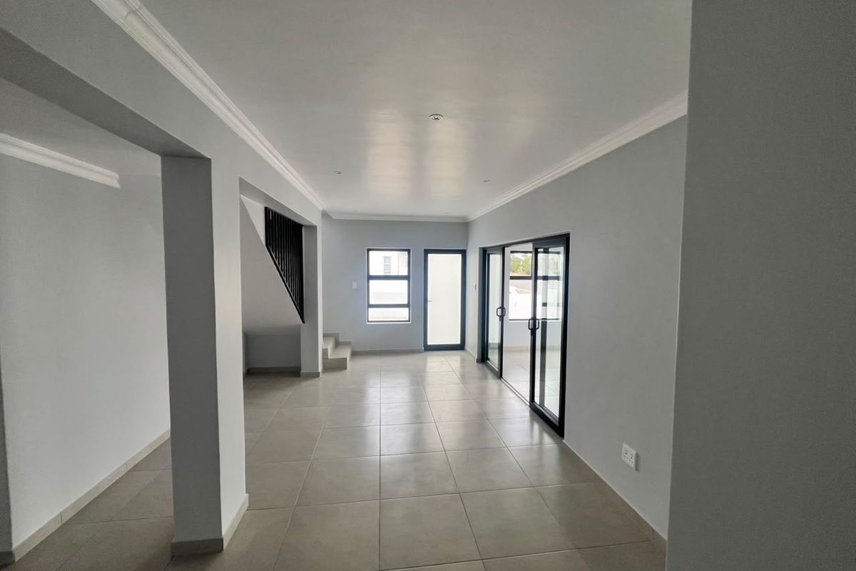 A spacious, open-plan living area featuring neutral tiled flooring, modern sliding glass doors, and a staircase with a contemporary metal balustrade.