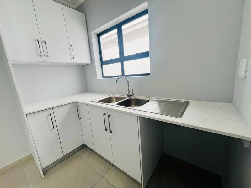 A clean and modern scullery featuring white built-in cabinetry, a stainless steel double sink, and stone countertops.