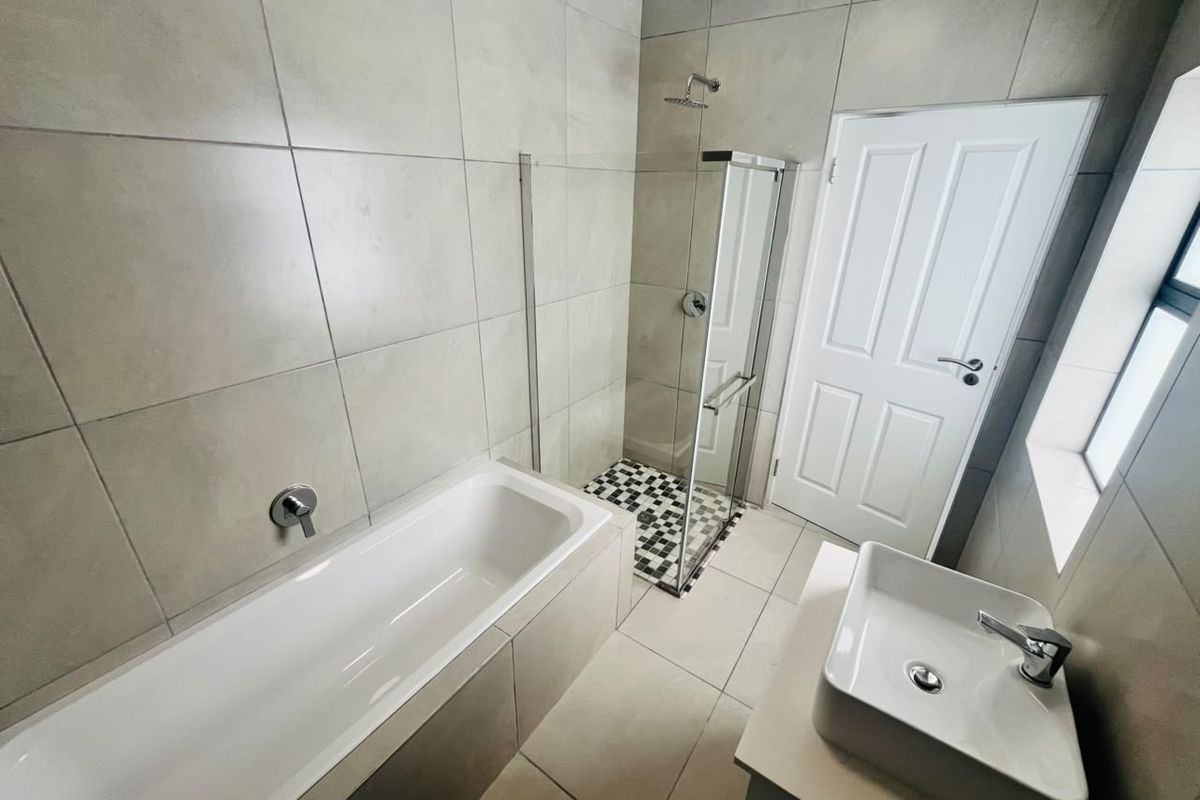 Modern bathroom featuring a built-in bathtub, separate glass-enclosed shower, and a contemporary vessel sink vanity with neutral floor-to-ceiling tiling.