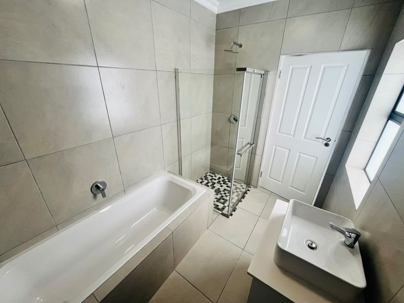 Modern bathroom featuring a built-in bathtub, separate glass-enclosed shower, and a contemporary vessel sink vanity with neutral floor-to-ceiling tiling.