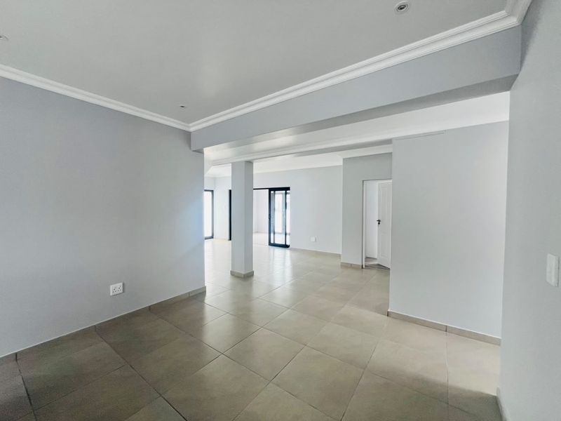 A spacious, light-filled open-plan living area featuring neutral tiled flooring, clean grey walls, and modern recessed lighting, offering a versatile blank canvas.