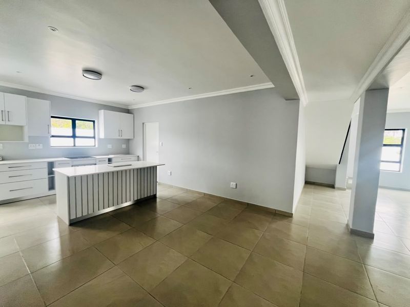 Spacious open-plan kitchen and living area featuring modern white cabinetry, a central island, tiled flooring, and neutral finishes throughout.
