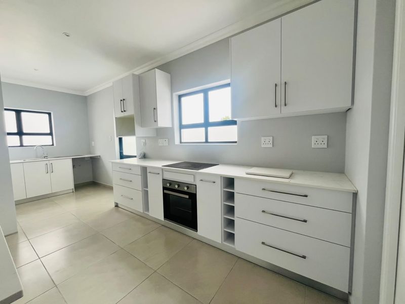 Modern, clean-lined kitchen featuring white cabinetry, stone countertops, integrated electric hob and oven, and neutral tiled flooring in an open-plan layout.