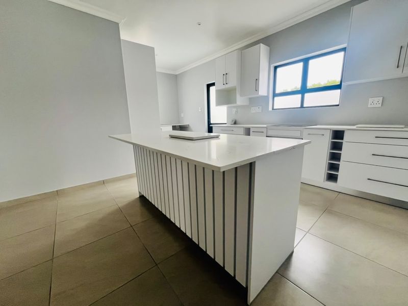 Modern, bright kitchen featuring a central island with quartz countertops, ample white cabinetry, and neutral tiled flooring in a clean, minimalist design.