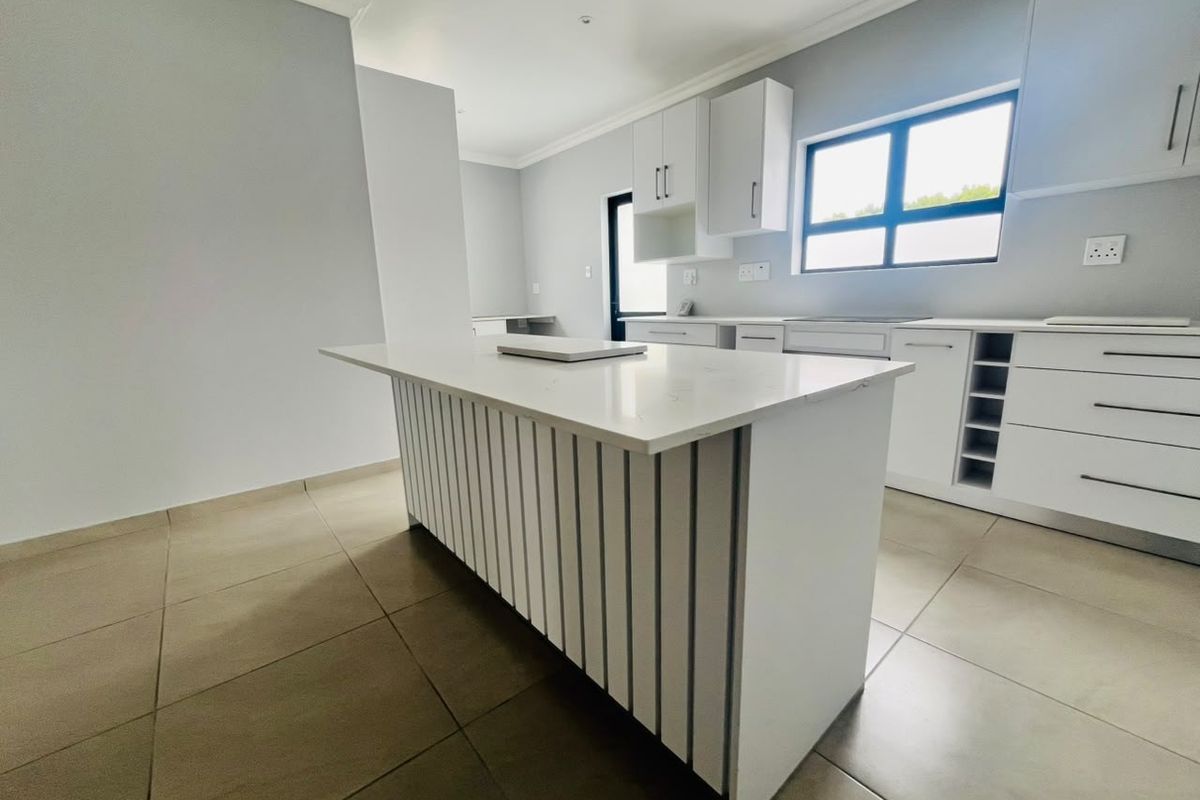 Modern, bright kitchen featuring a central island with quartz countertops, ample white cabinetry, and neutral tiled flooring in a clean, minimalist design.