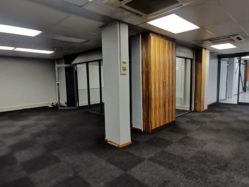 Spacious open-plan office area featuring suspended ceilings, recessed lighting, central air conditioning, glass partitions, and built-in storage cabinetry.