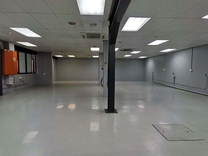 A spacious, open-plan office area featuring polished epoxy flooring, suspended ceilings with recessed lighting, and integrated air conditioning units.