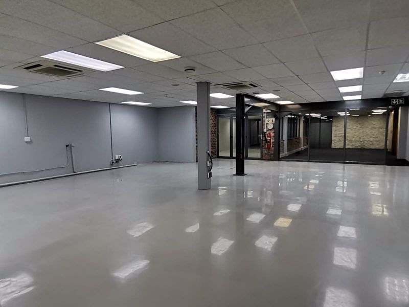 Spacious open-plan office area featuring polished epoxy flooring, suspended ceilings with recessed lighting, and modern glass partitions.