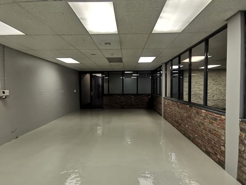A spacious, empty office area featuring polished epoxy flooring, exposed brick accents, glass partitions, and a suspended ceiling with recessed lighting.