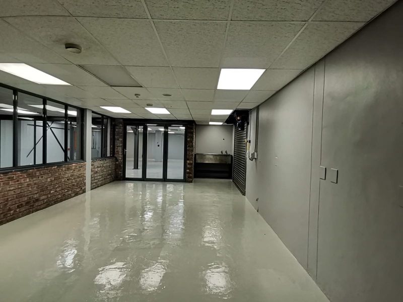 A spacious, empty office area featuring polished epoxy flooring, exposed brick accents, a suspended ceiling with recessed lighting, and a secure metal roller shutter.