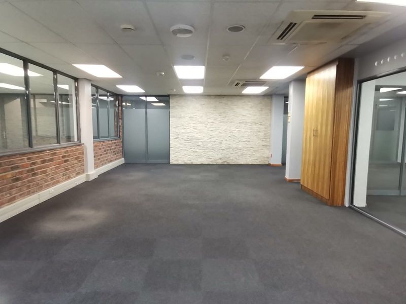 A spacious, empty office area featuring a mix of exposed brick and stone wall finishes, glass partitions, built-in cabinetry, and modern recessed ceiling lighting.