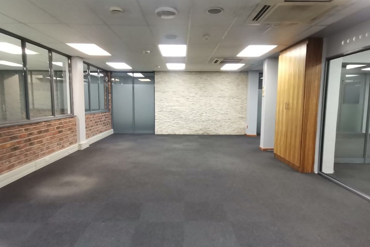 A spacious, empty office area featuring a mix of exposed brick and stone wall finishes, glass partitions, built-in cabinetry, and modern recessed ceiling lighting.
