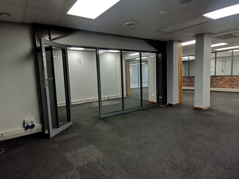 Open-plan office space featuring glass partitions, exposed brick accents, structural columns, and recessed lighting, providing a versatile and professional work environment.