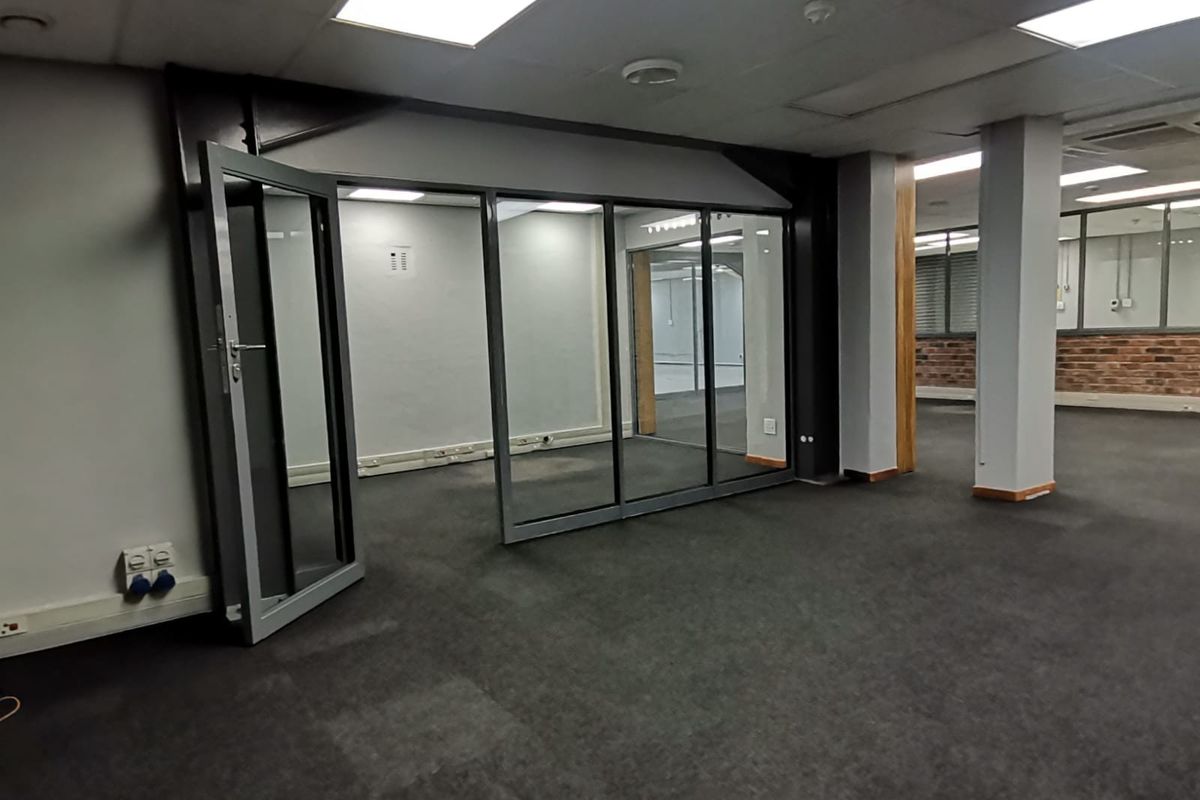 Open-plan office space featuring glass partitions, exposed brick accents, structural columns, and recessed lighting, providing a versatile and professional work environment.