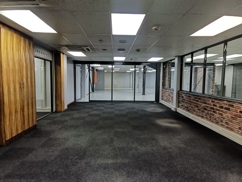 Spacious open-plan office area featuring glass partitions, exposed brick accents, built-in storage cabinetry, and a suspended ceiling with integrated lighting.