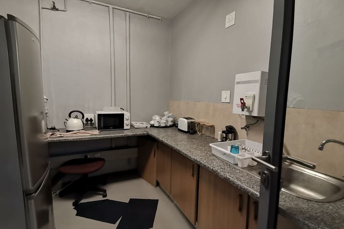 A compact office kitchenette featuring granite countertops, built-in cabinetry, a stainless steel sink, and a wall-mounted water dispenser.