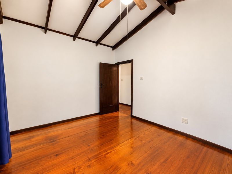 A bright, empty bedroom featuring polished timber flooring, exposed dark timber ceiling beams, and a ceiling fan, offering a clean and neutral living space.