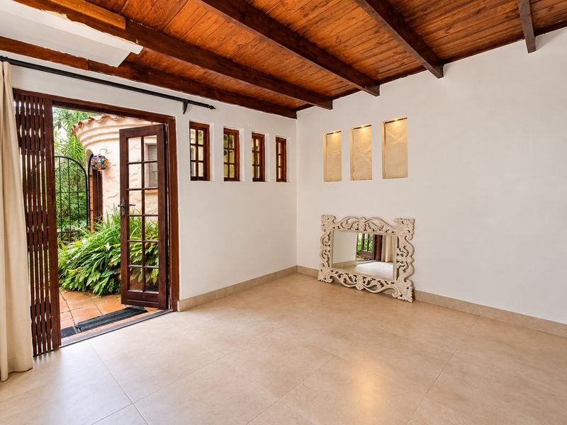 Bright living area featuring exposed timber beam ceilings, tiled flooring, and recessed wall niches, with direct access to an outdoor patio area.