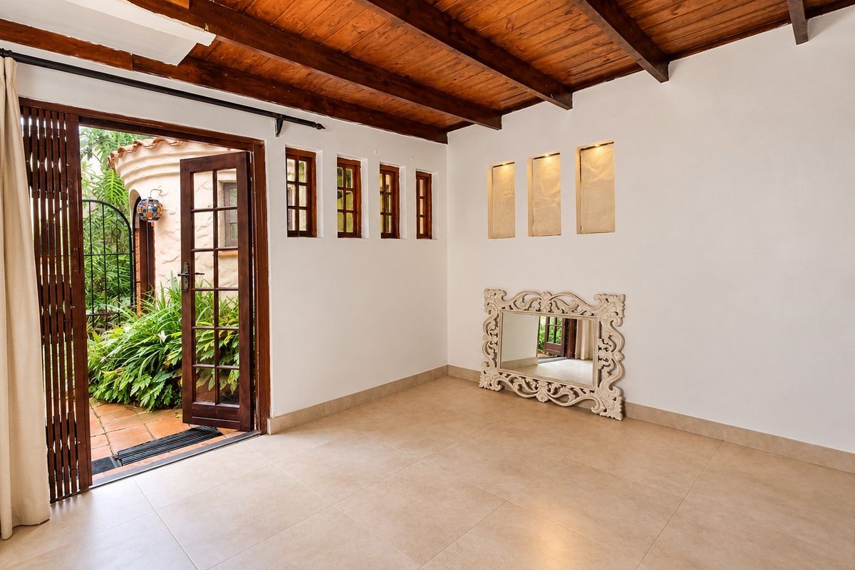 Bright living area featuring exposed timber beam ceilings, tiled flooring, and recessed wall niches, with direct access to an outdoor patio area.