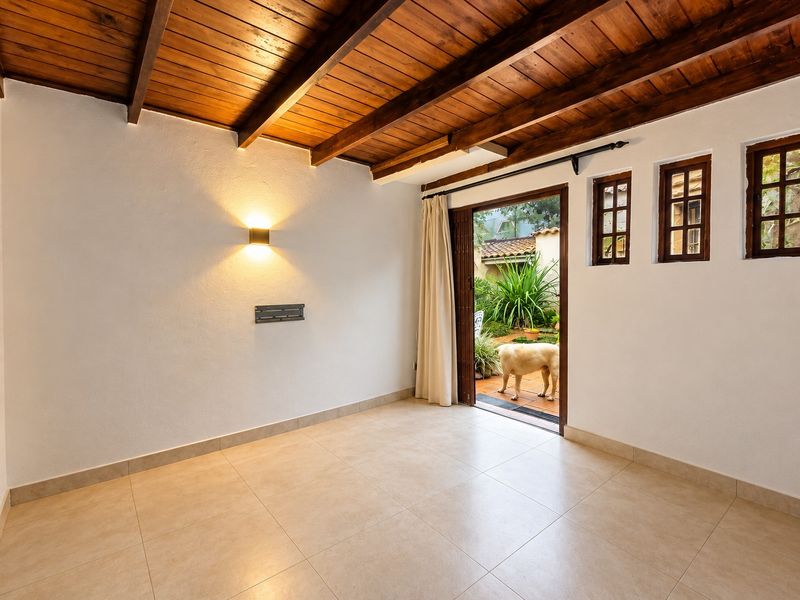 A bright, empty living room featuring exposed timber ceiling beams, tiled flooring, and direct access to an outdoor patio area.