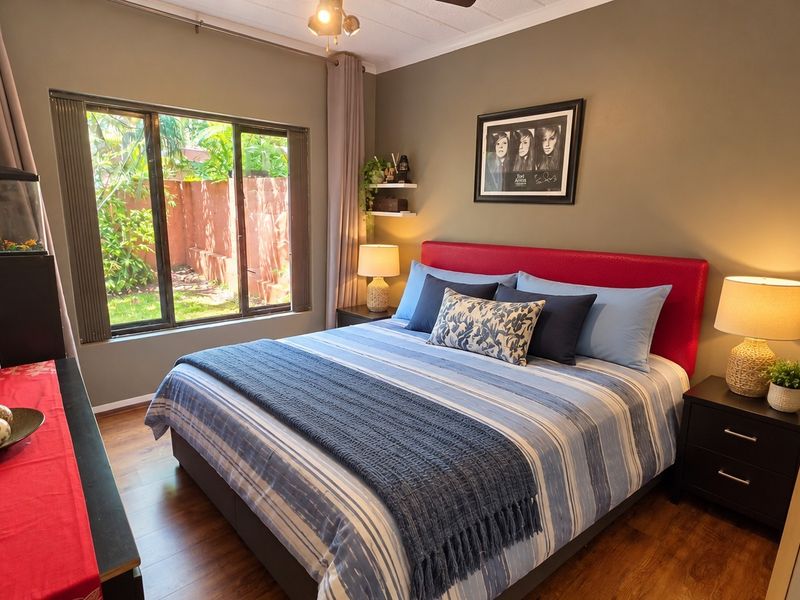 A well-maintained bedroom featuring laminate flooring, a large window providing natural light, and a ceiling fan.