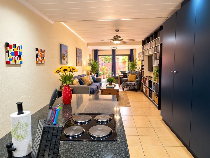 Open-plan living area featuring a modern kitchen with granite countertops, electric hob, extensive built-in cabinetry, and seamless flow to a rear patio.