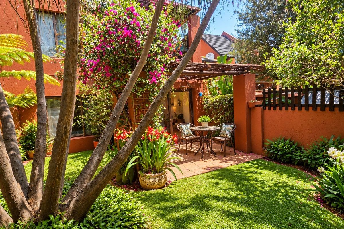 A private rear garden featuring a terracotta paved patio area, a timber pergola, and established landscaping against a terracotta-colored building facade.