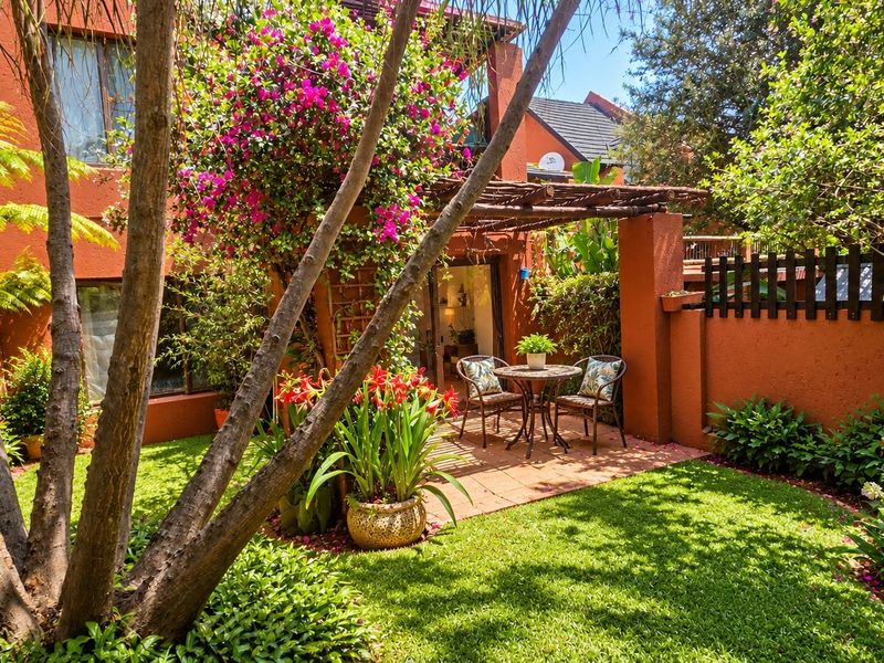 A private rear garden featuring a terracotta paved patio area, a timber pergola, and established landscaping against a terracotta-colored building facade.