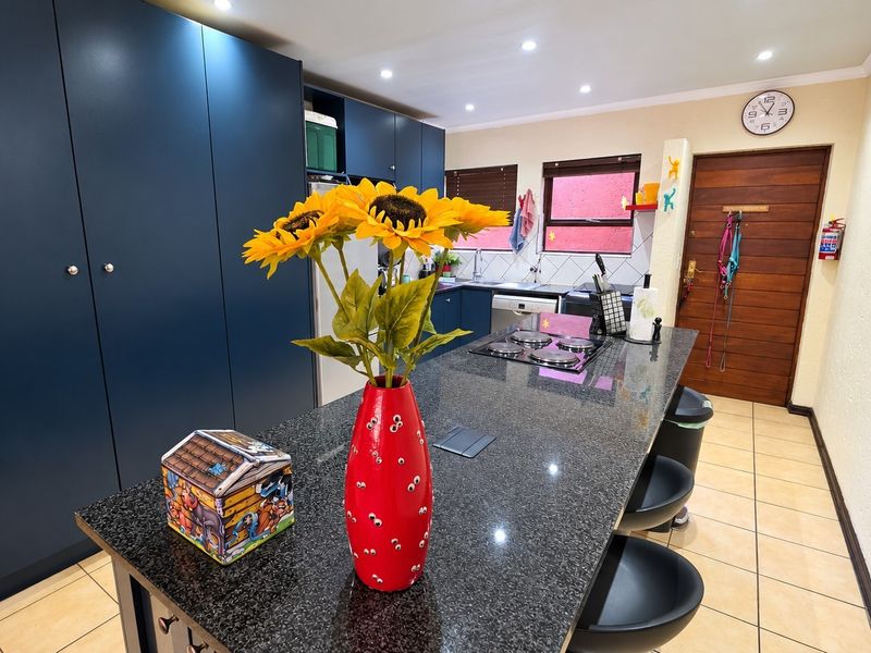 Modern kitchen featuring a large granite island with built-in hob, dark blue cabinetry, and tiled flooring.