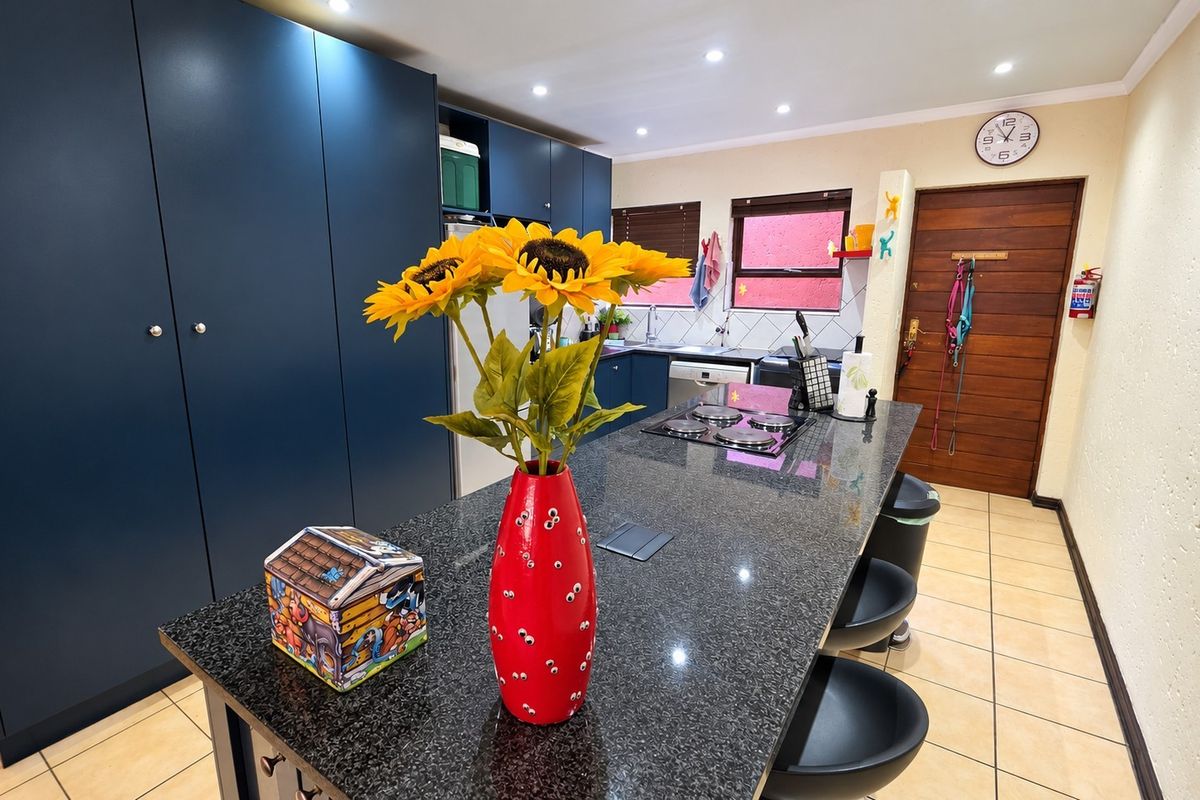Modern kitchen featuring a large granite island with built-in hob, dark blue cabinetry, and tiled flooring.